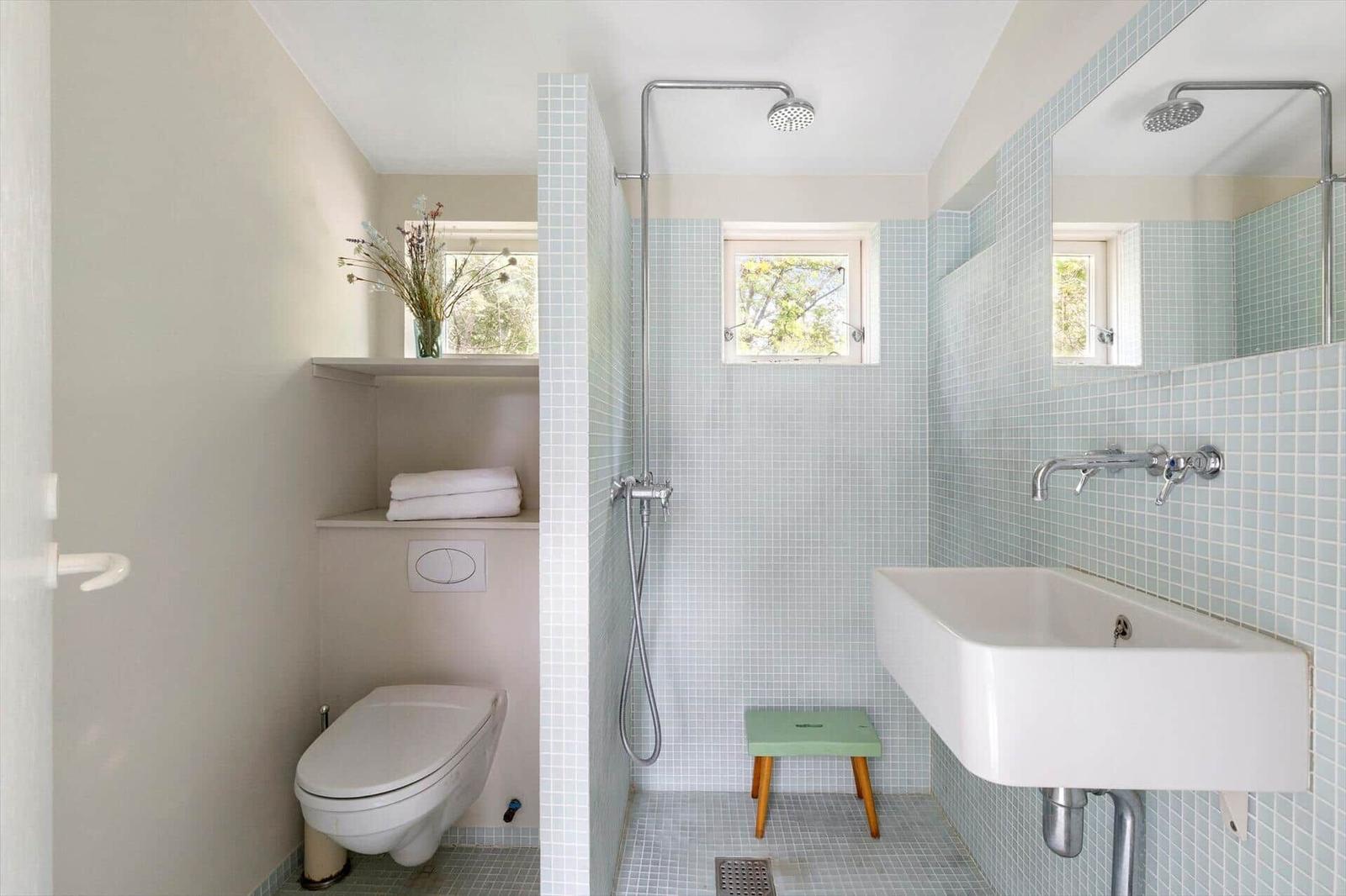 Bathroom with shower, sink, and toilet. Wall tiles and window visible.