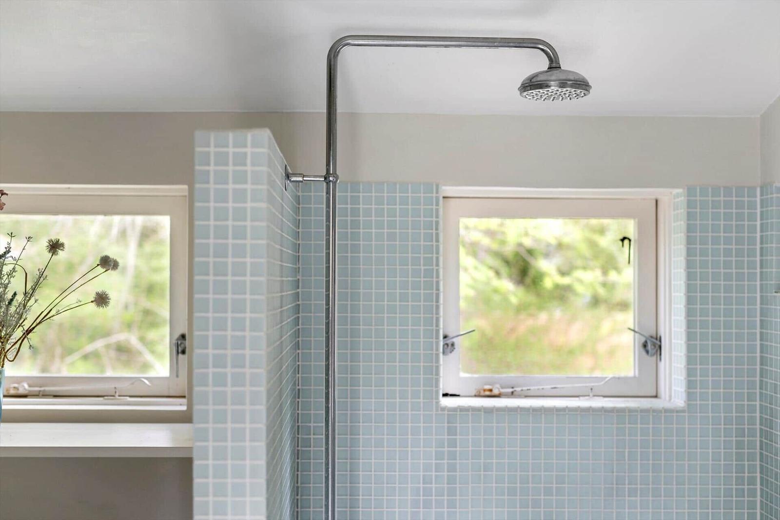 Shower cabin with blue tiles and two windows. Showerhead on the ceiling.