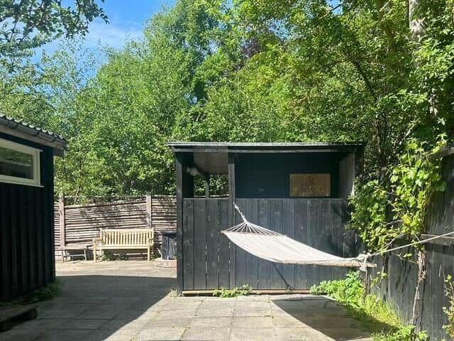 Hammock seating area in front of a wooden shed with garden and trees.