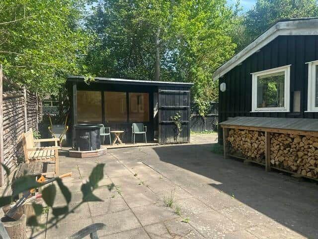 Backyard with pavilion, seating, and firewood stack beside a black house.