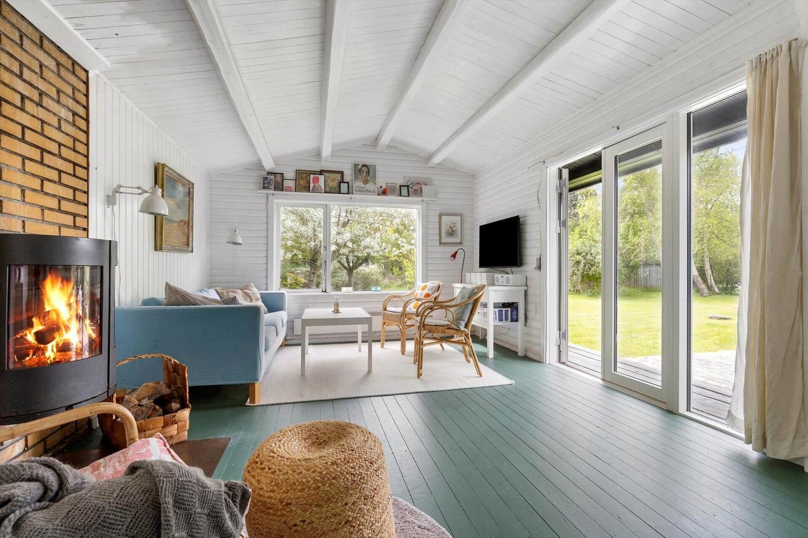 Living room with fireplace, sofa, TV, and terrace. Wooden floor and white walls.