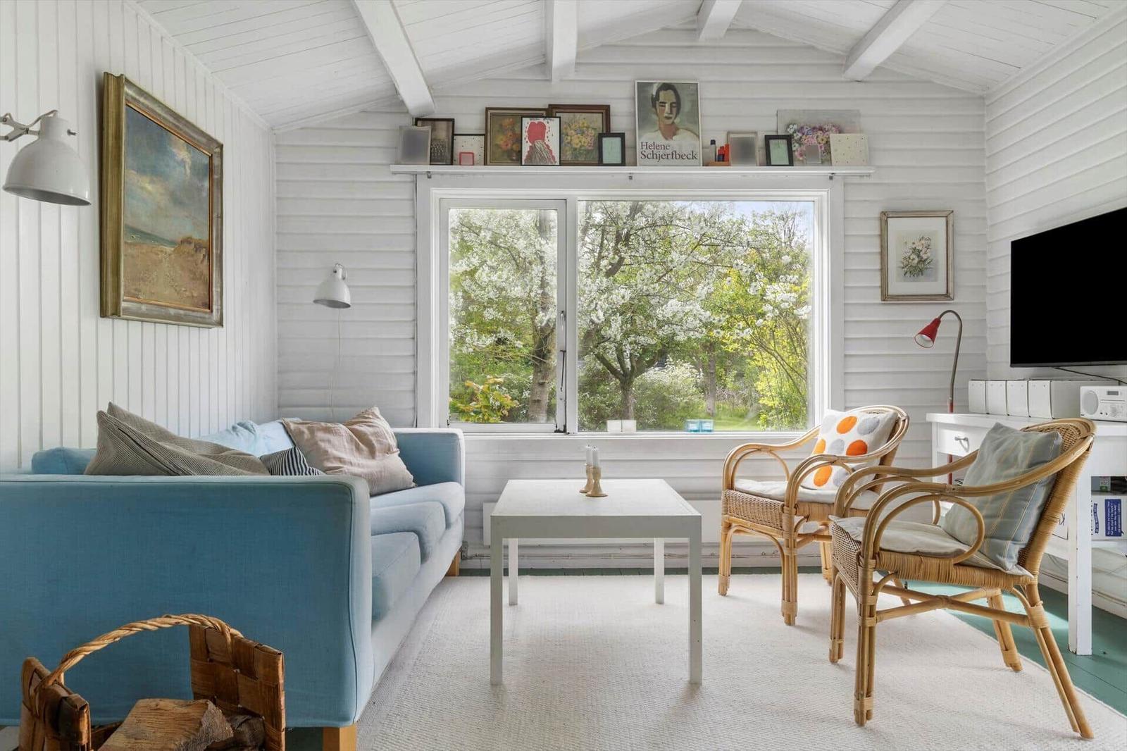 A living room with a blue sofa, two rattan chairs, and a large window overlooking trees.
