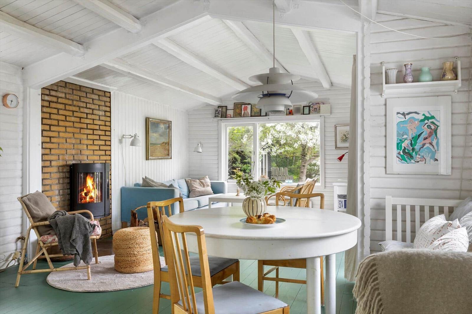 A room with dining area, sofa, and fireplace. Wooden ceiling, white walls, and green floor.