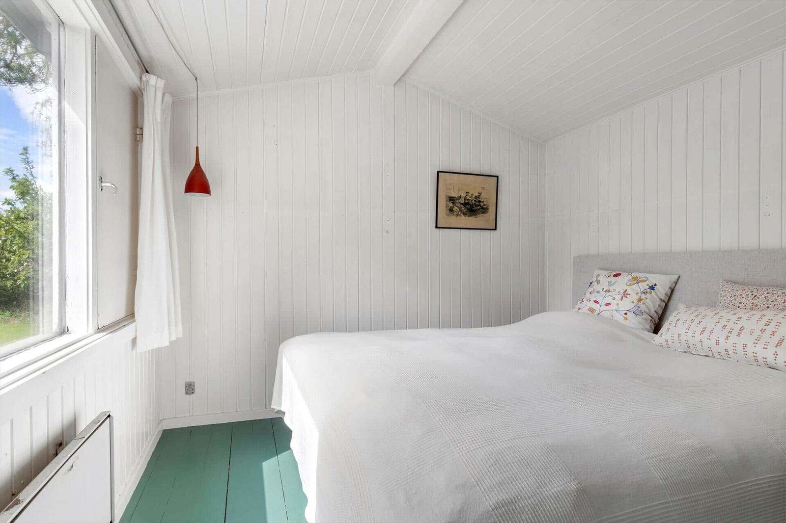 Bedroom with white panel walls, bed, and window with view outside.