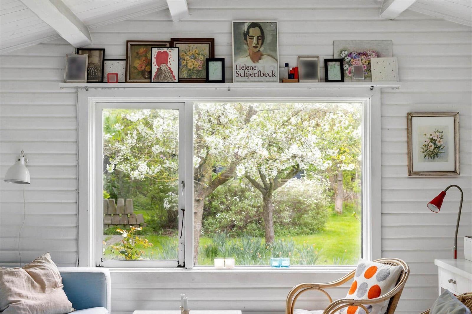 A room with white wood paneling, large window, and view of blooming trees. Candles sit on the sill.