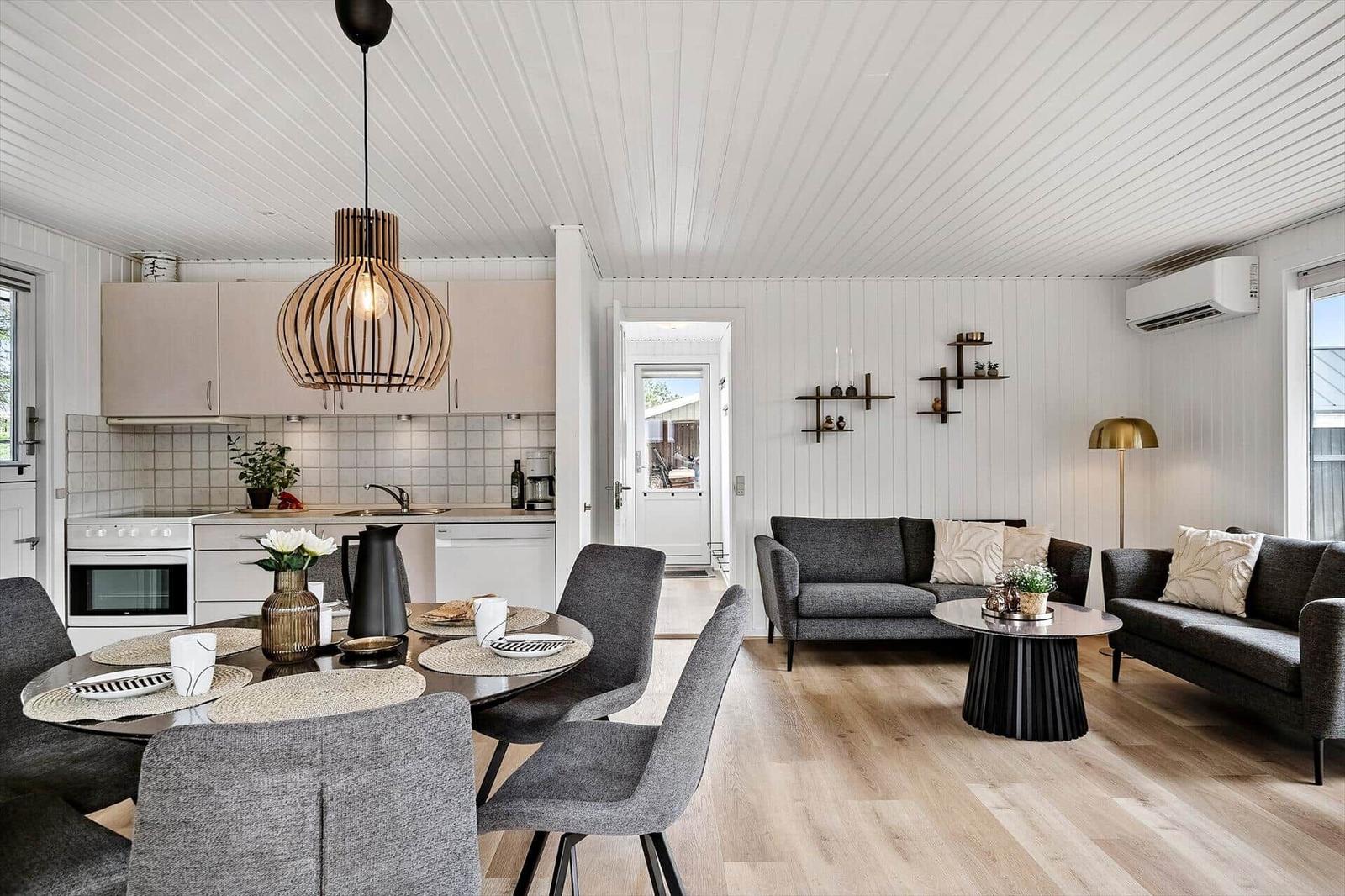 Küche, Essbereich und Wohnzimmer mit grauen Sofas, Holzboden und weißer Wandverkleidung.
