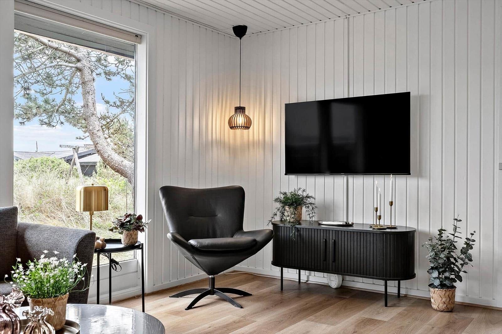 Ein Wohnzimmer mit schwarzer Sitzgelegenheit, Fernseher und Pflanzen an weiß verkleideten Wänden.