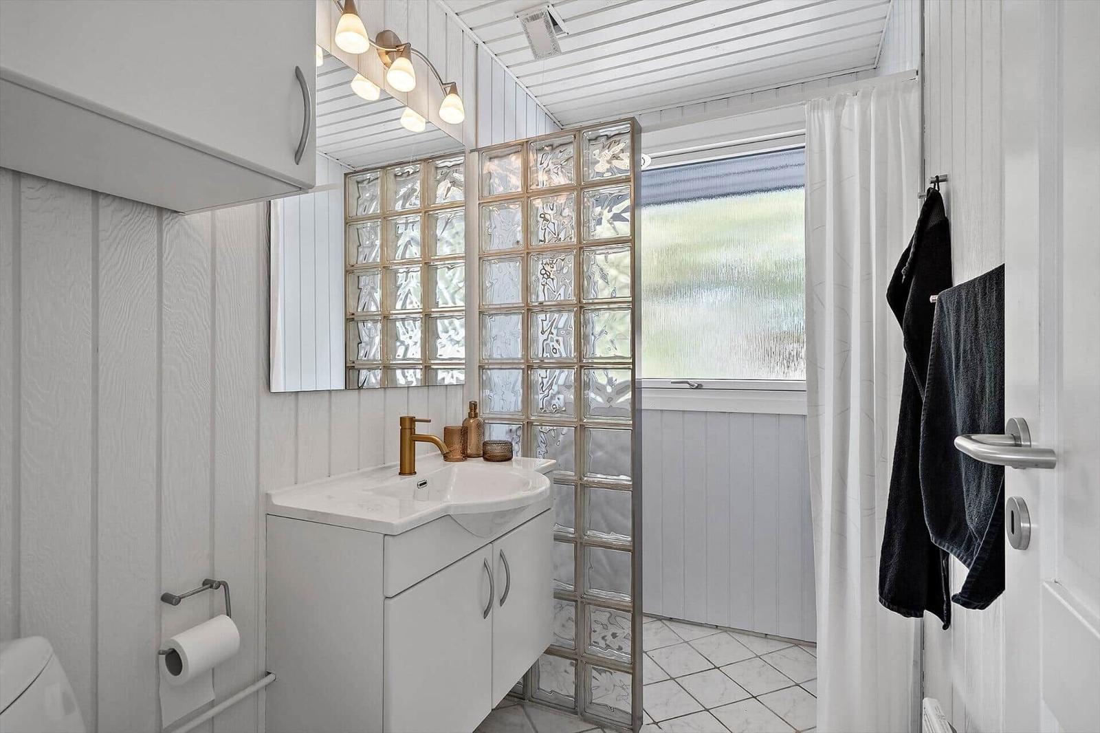 Badezimmer mit Waschbecken, Spiegel, Glaswand und Fenster.