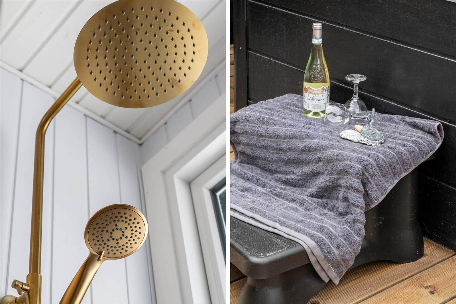 Goldfarbene Duschkopf und Handbrause an weißer Wand. Auf grauer Decke steht eine Weinflasche und Gläser.