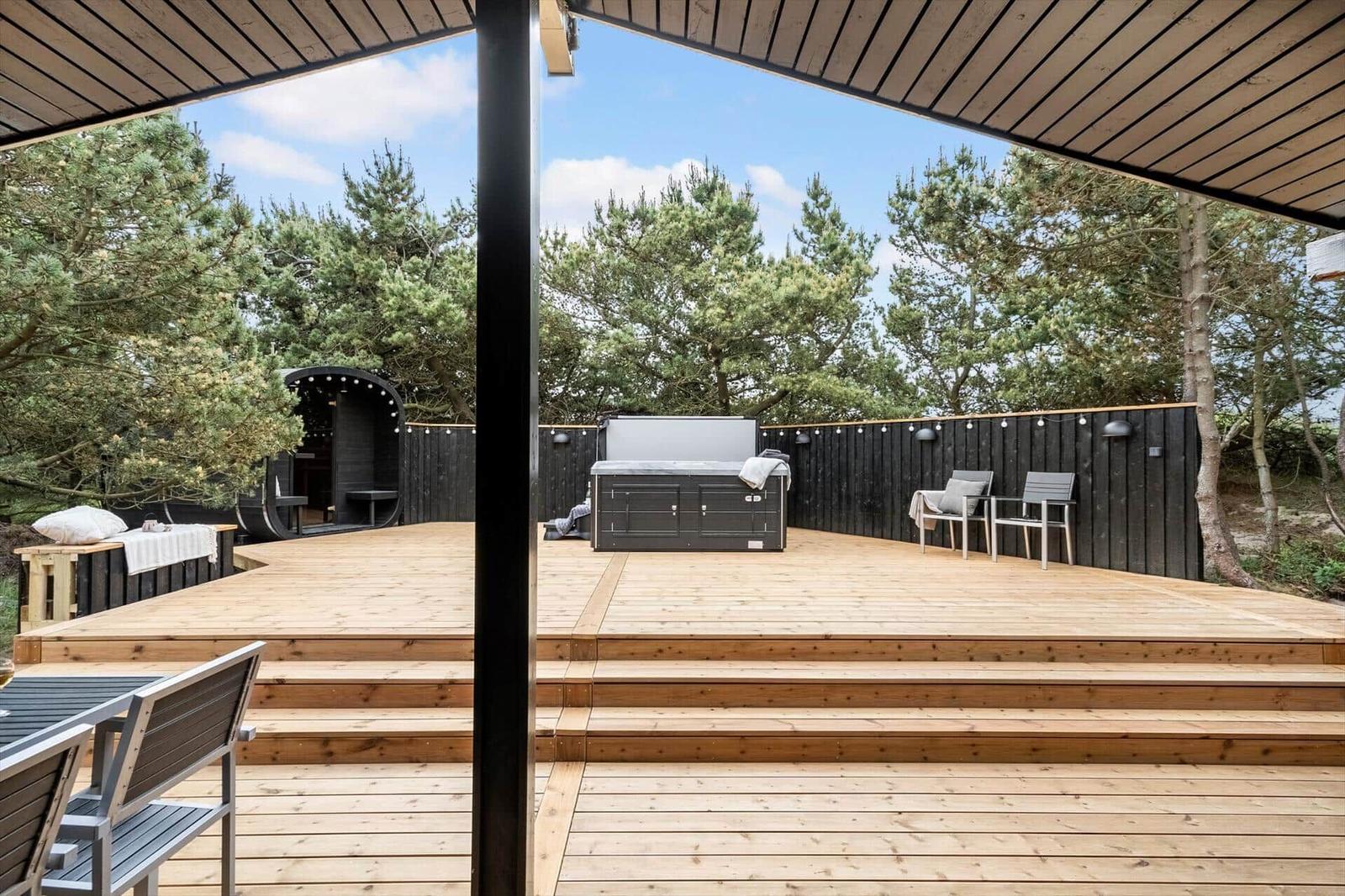 Holzterrasse mit Whirlpool, Sitzgelegenheiten und Blick auf Bäume.