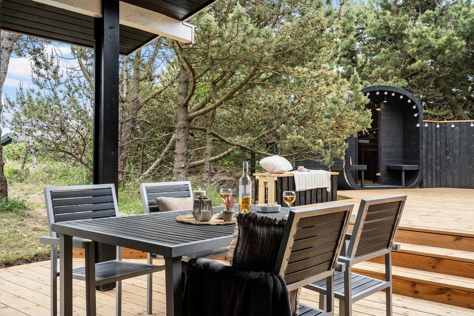Terrasse mit Tisch und Stühlen, Sauna im Hintergrund, umgeben von Bäumen.