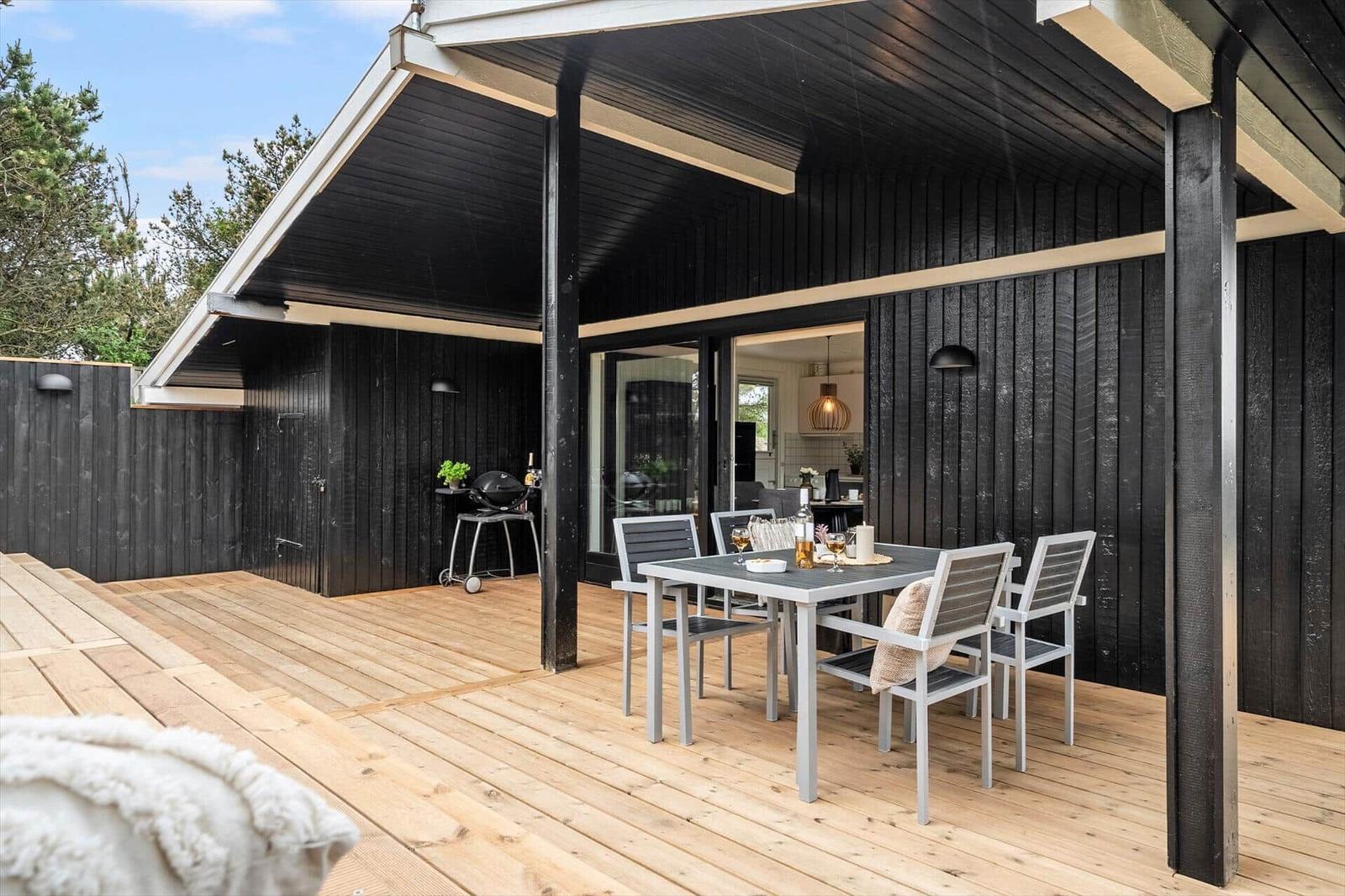 Terrasse mit Essgruppe, Grill und Blick ins Haus. Holzdecke und schwarze Wandverkleidung.