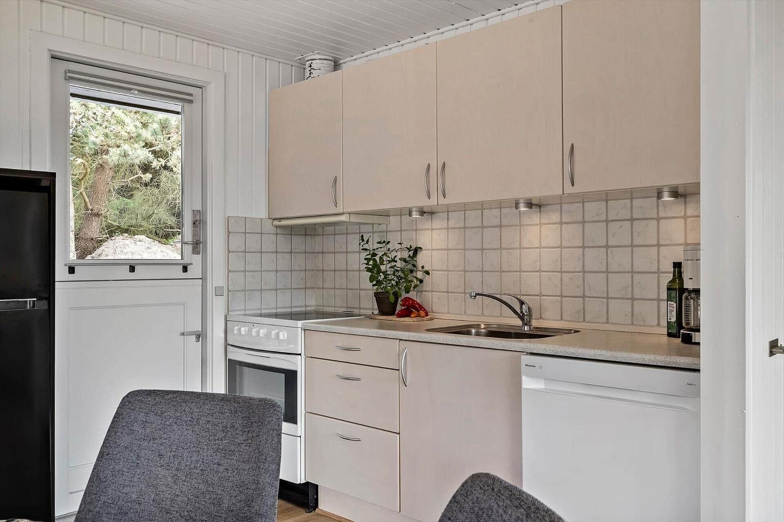 Küche mit hellen Schränken, Spüle, Herd und Fenster zum Garten.