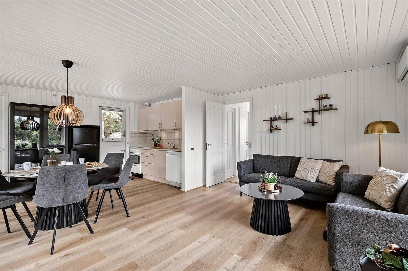 Wohn- und Essbereich mit Küche, Sofa und Esstisch. Holzboden und weiße Wände.