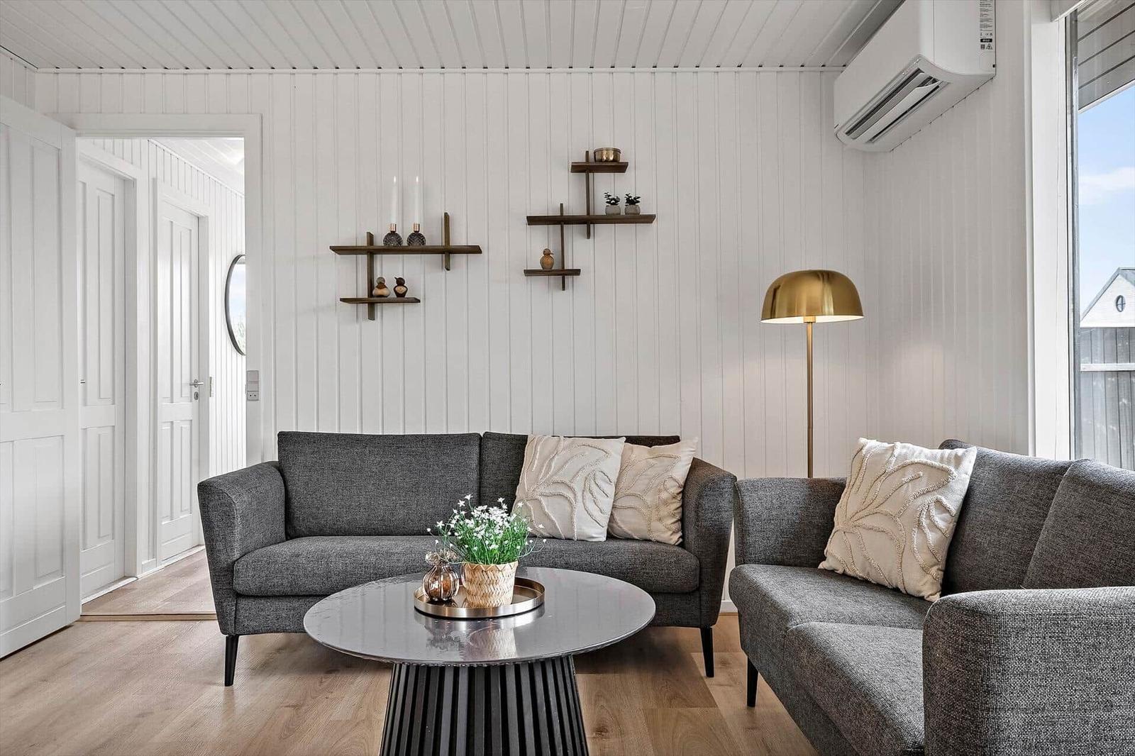 Wohnzimmer mit grauem Sofa, runden Tisch und Wandregalen.