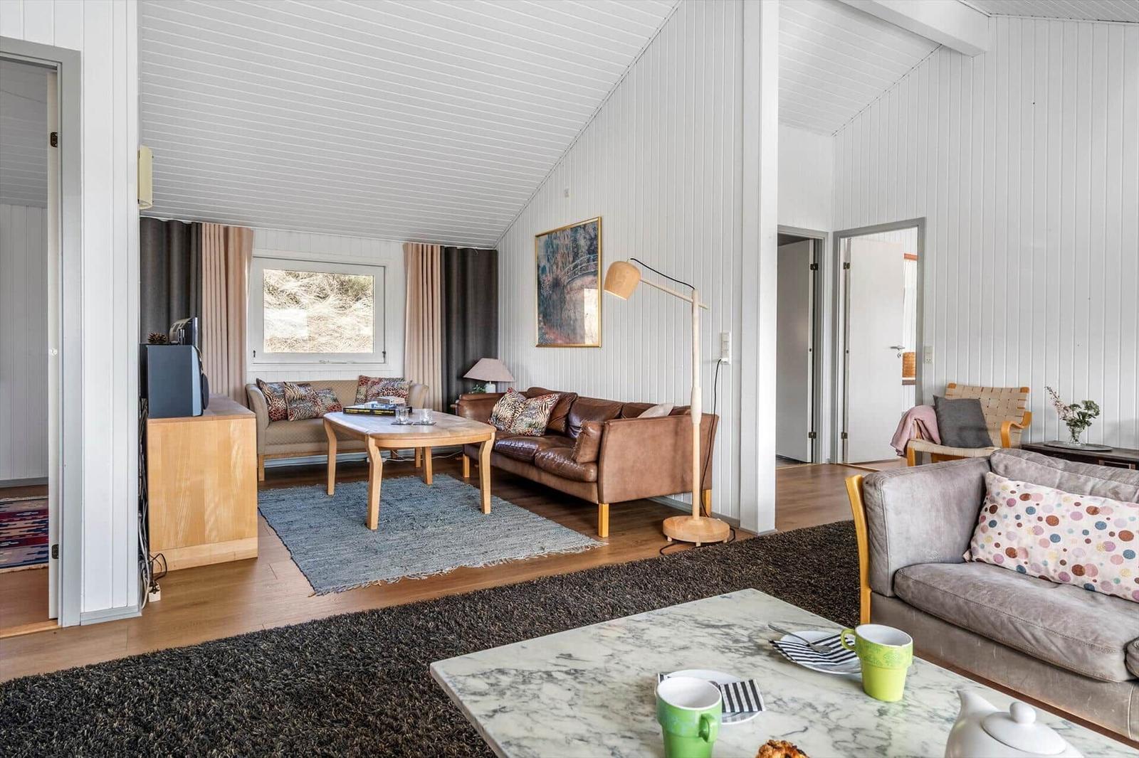 Wohnzimmer mit Sofa, Couchtisch und Fenster. Holzfußboden und weiße Wände.