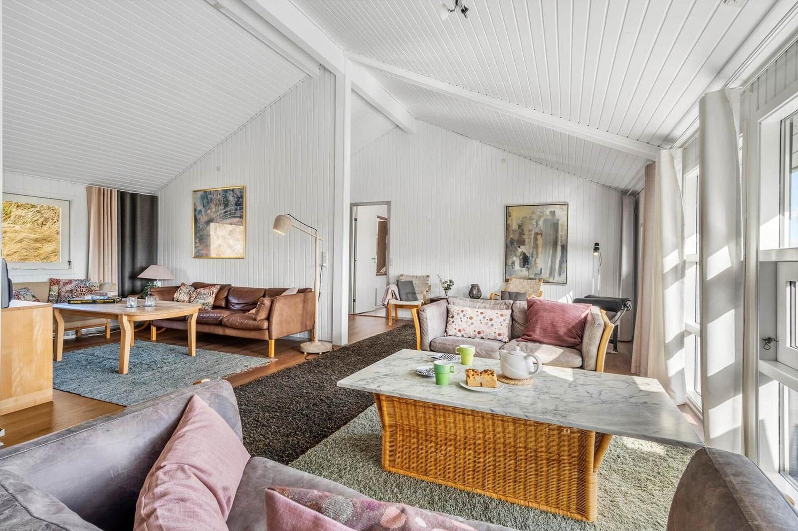 Wohnzimmer mit Sofa, Tisch und Fenstern. Decke und Wände sind weiß.