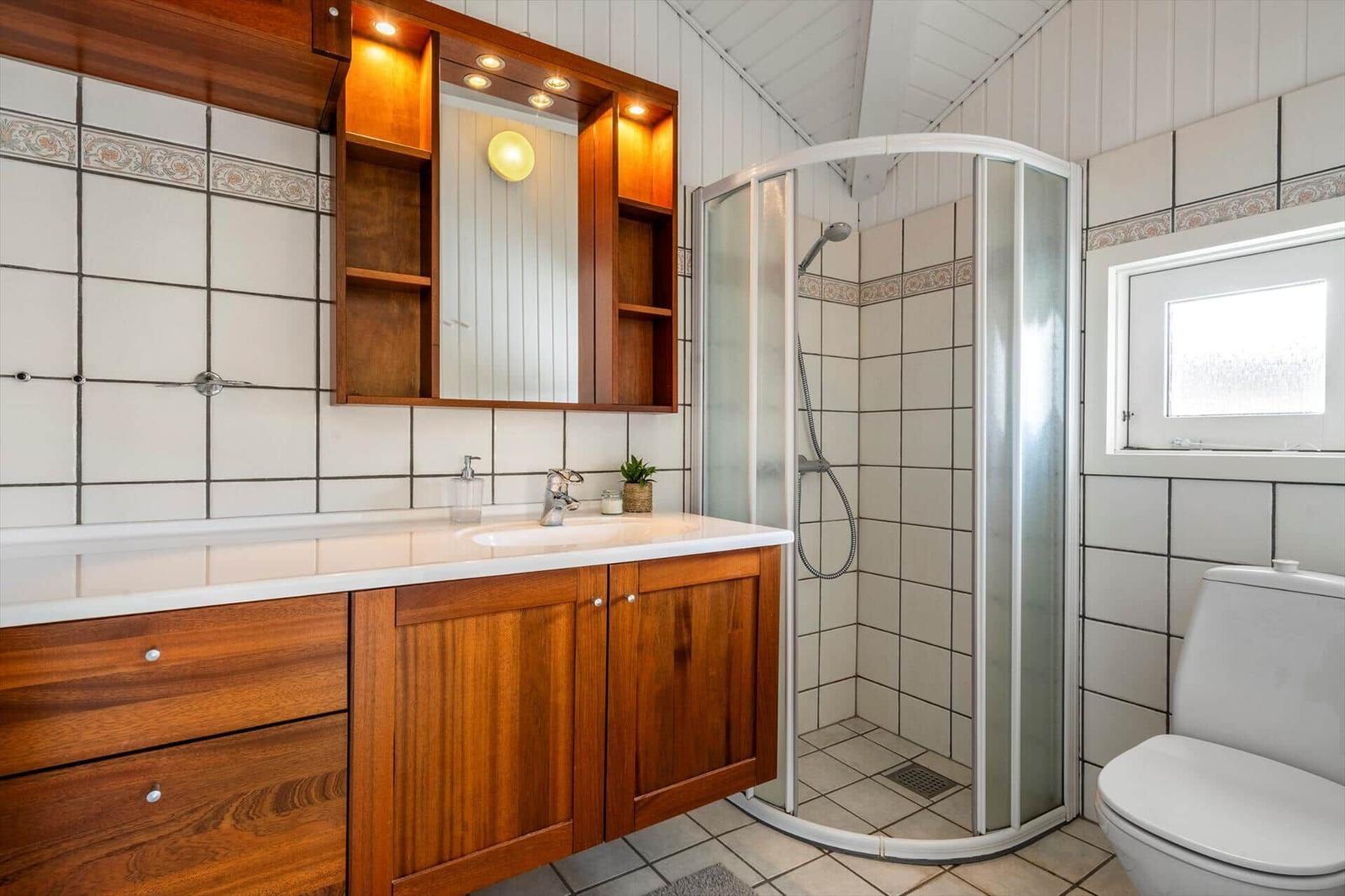 Badezimmer mit Dusche, Waschbecken und Toilette. Holzschrank und Fliesenwand.