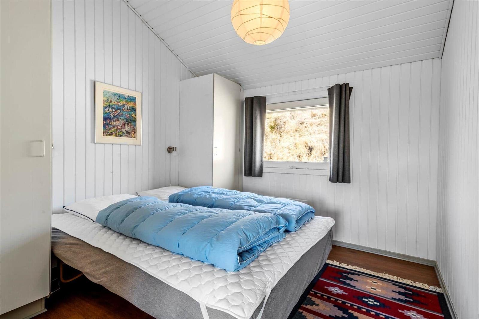 Schlafzimmer mit Bett, Wandbild und Fenster mit Vorhängen.
