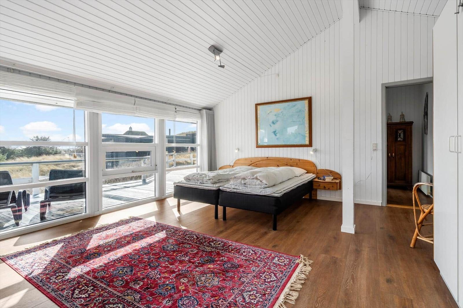 Schlafzimmer mit Doppelbett, Holzboden und großem Fensterblick auf Terrasse.