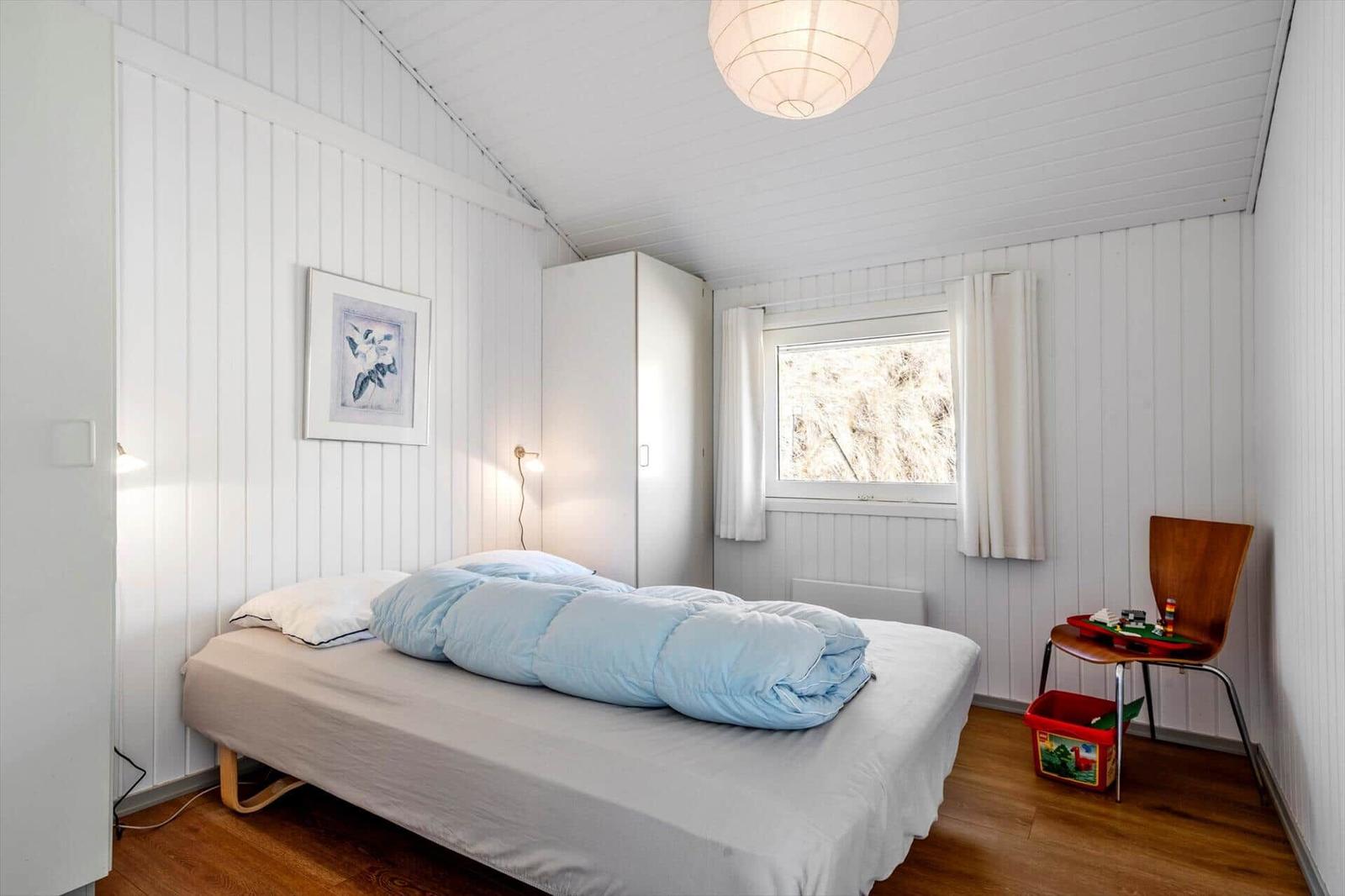 Schlafzimmer mit Bett, Kleiderschrank, Fenster und Stuhl mit Spielzeug.