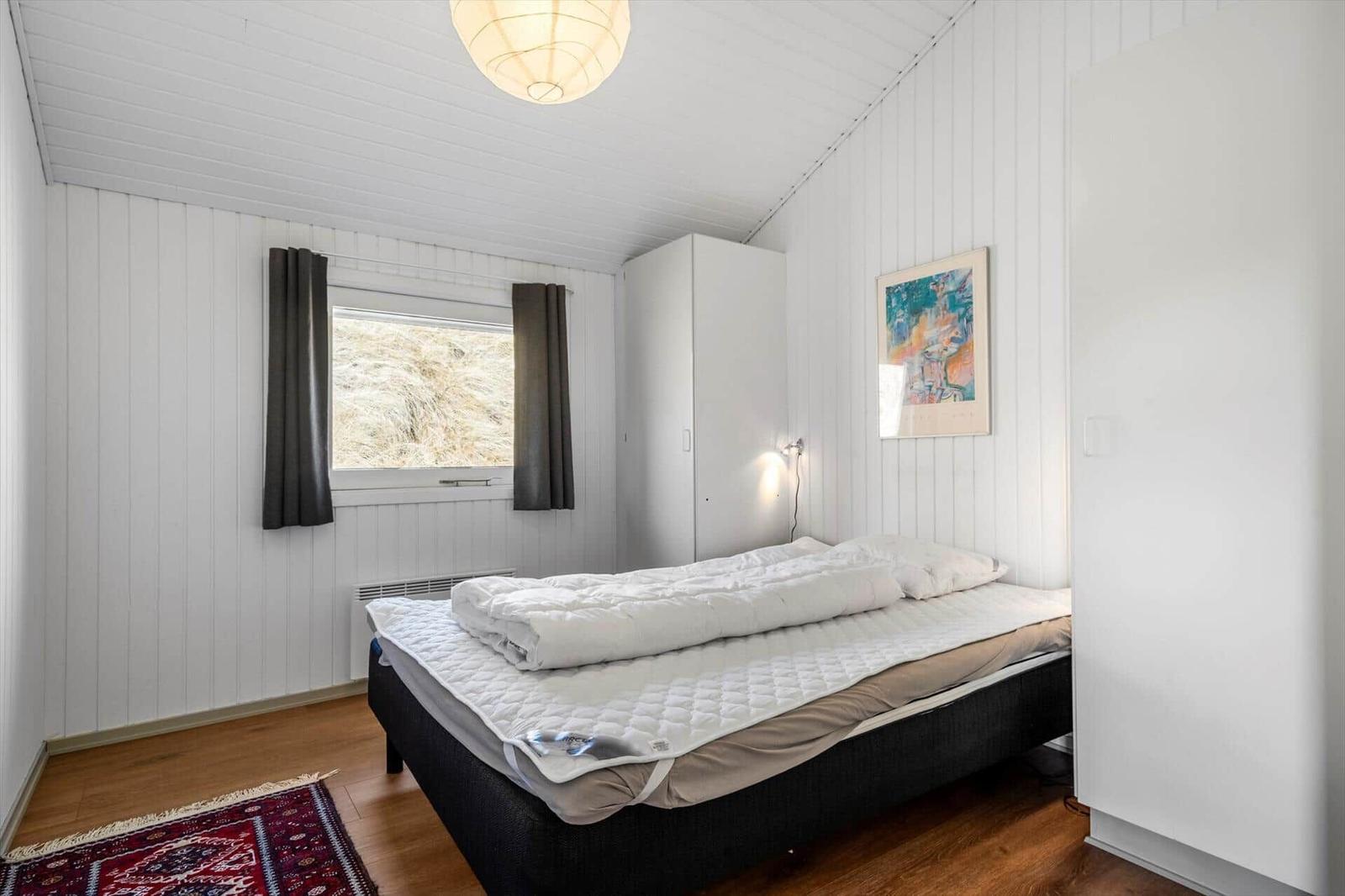 Schlafzimmer mit Bett, Kleiderschrank und Fenster mit Blick auf Gras.