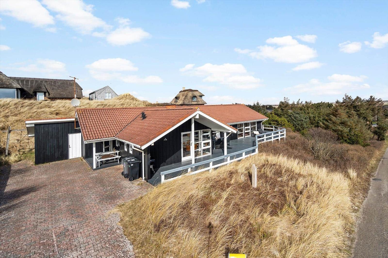 Ein Haus mit rotem Dach und Holzfassade auf einer Düne mit Blick auf andere Häuser.