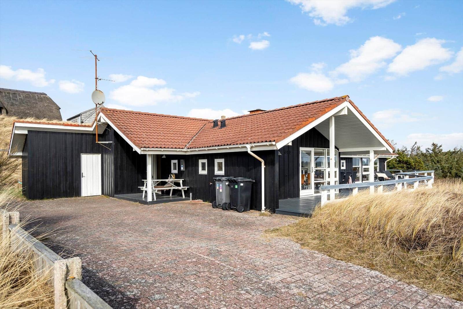 Schwarzes Holzhaus mit rotem Dach, Terrasse und Picknicktisch im Freien.