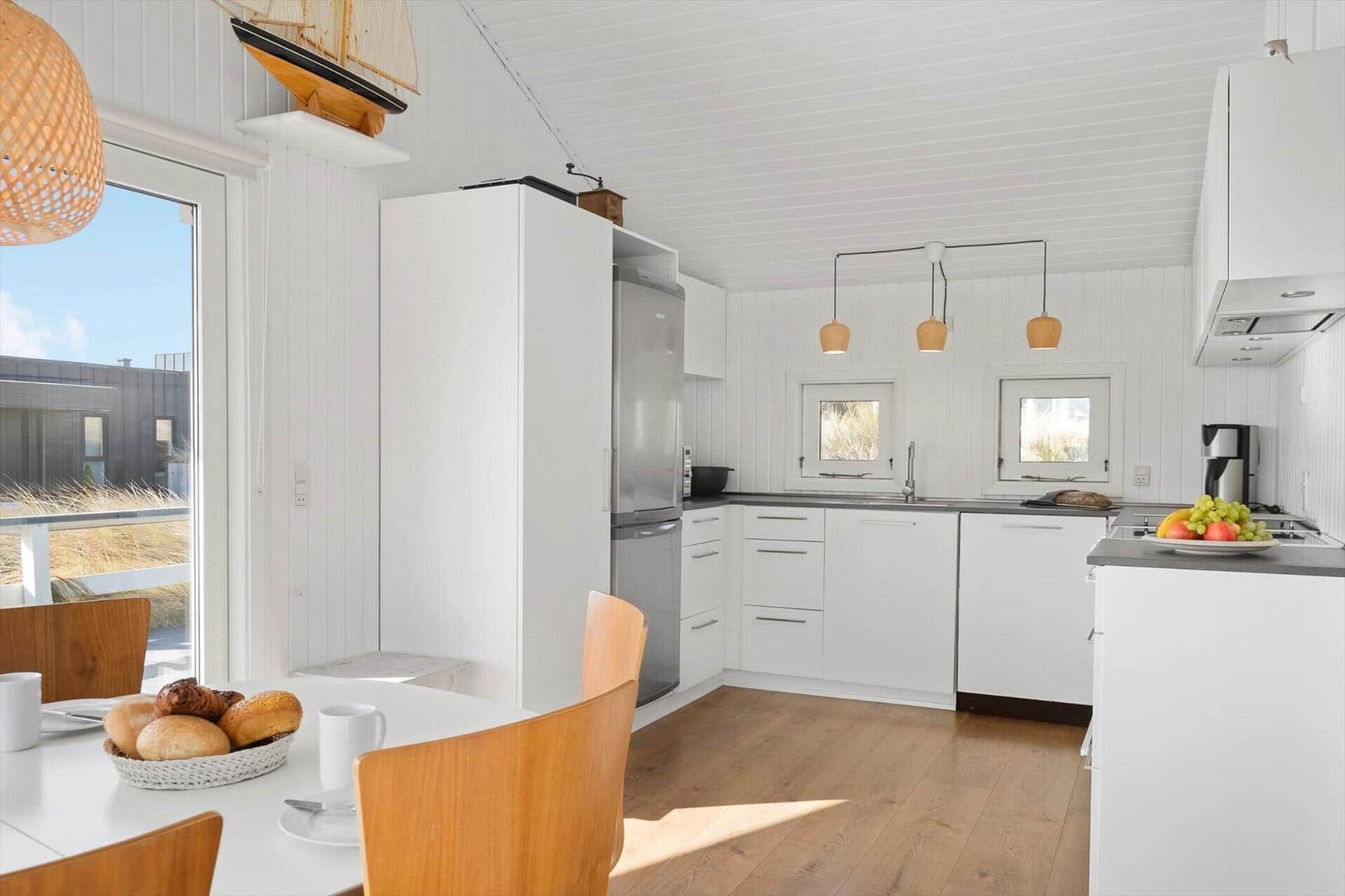 Küche mit Essbereich, weißen Schränken und Holzboden. Fenster und Deckenleuchten sorgen für Licht.