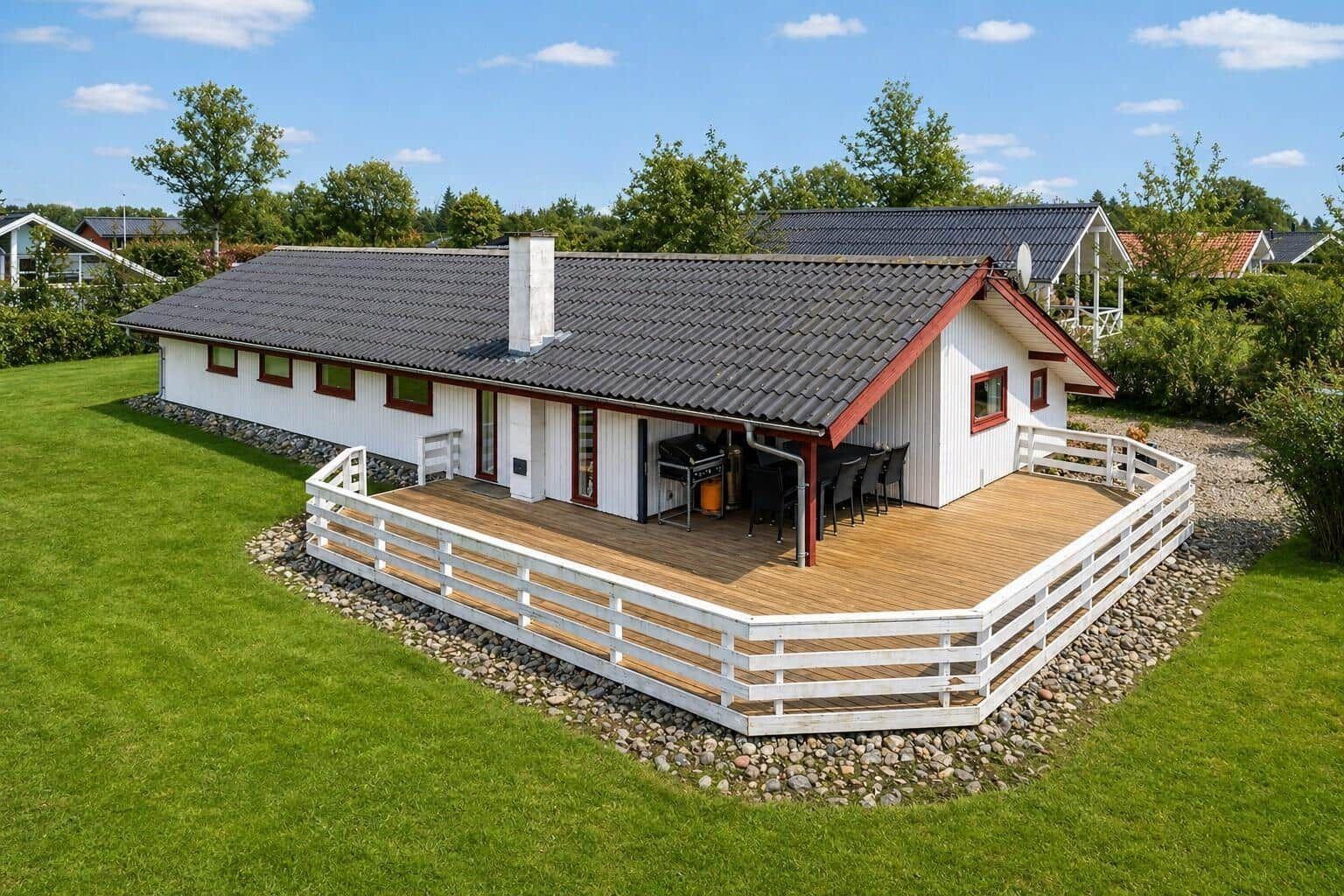 A house with a terrace, grill, and garden. White facade, red accents, and gray roof.