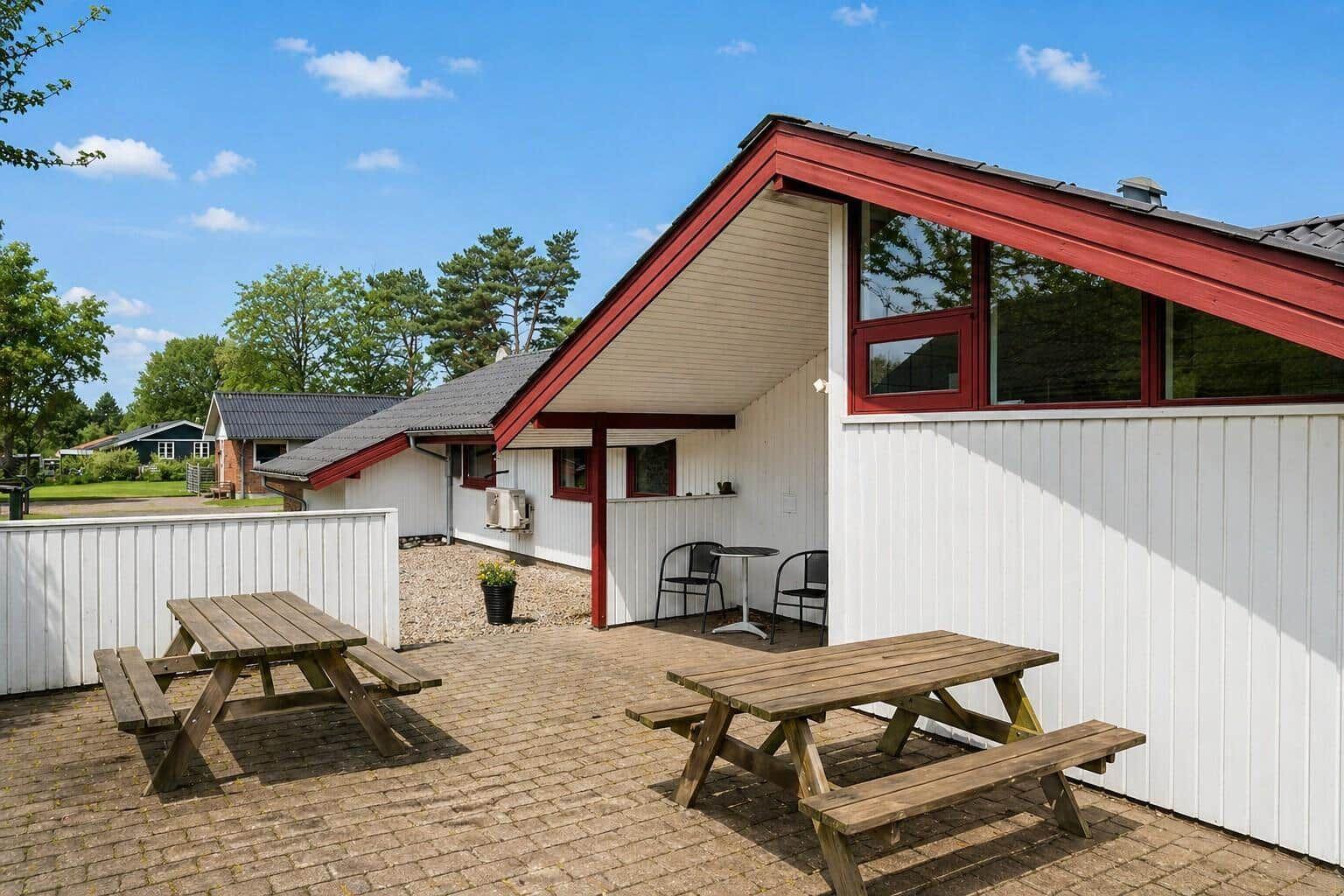 Terrace with two wooden tables and chairs in front of a white house with a red roof.