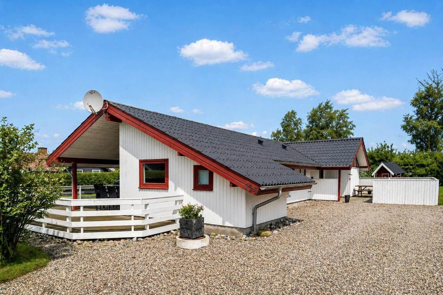 A white holiday home with a red roof and terrace under a blue sky.