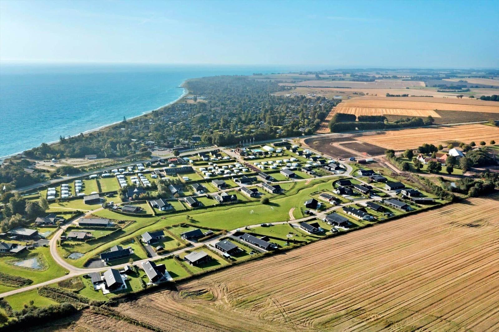 Aerial view of a coastal holiday park with cabins, campsites, and adjacent fields.
