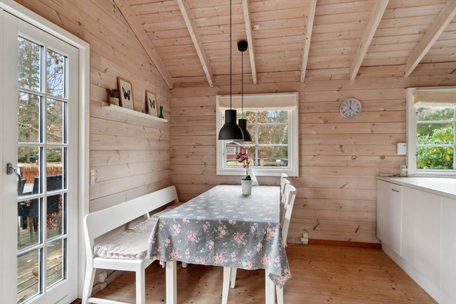 Wooden house with kitchen, dining table, and seating. White furniture and windows.