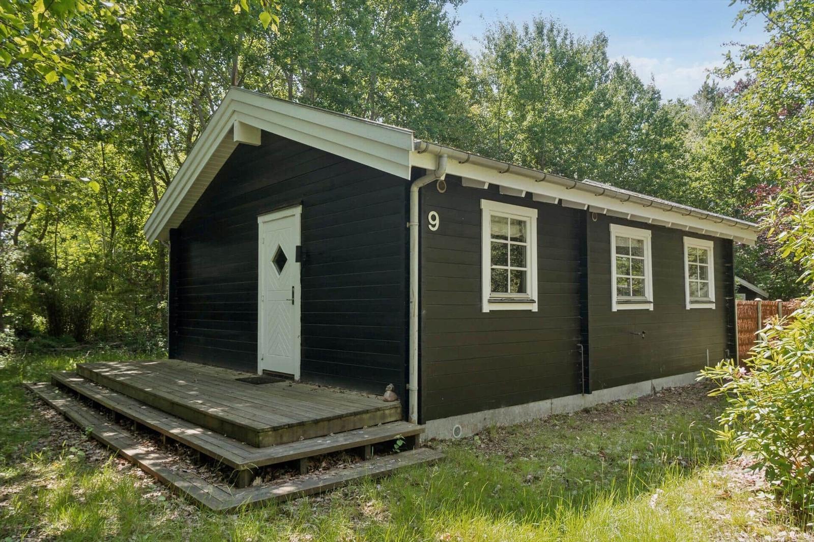 Black wooden house with white windows and terrace in the green.