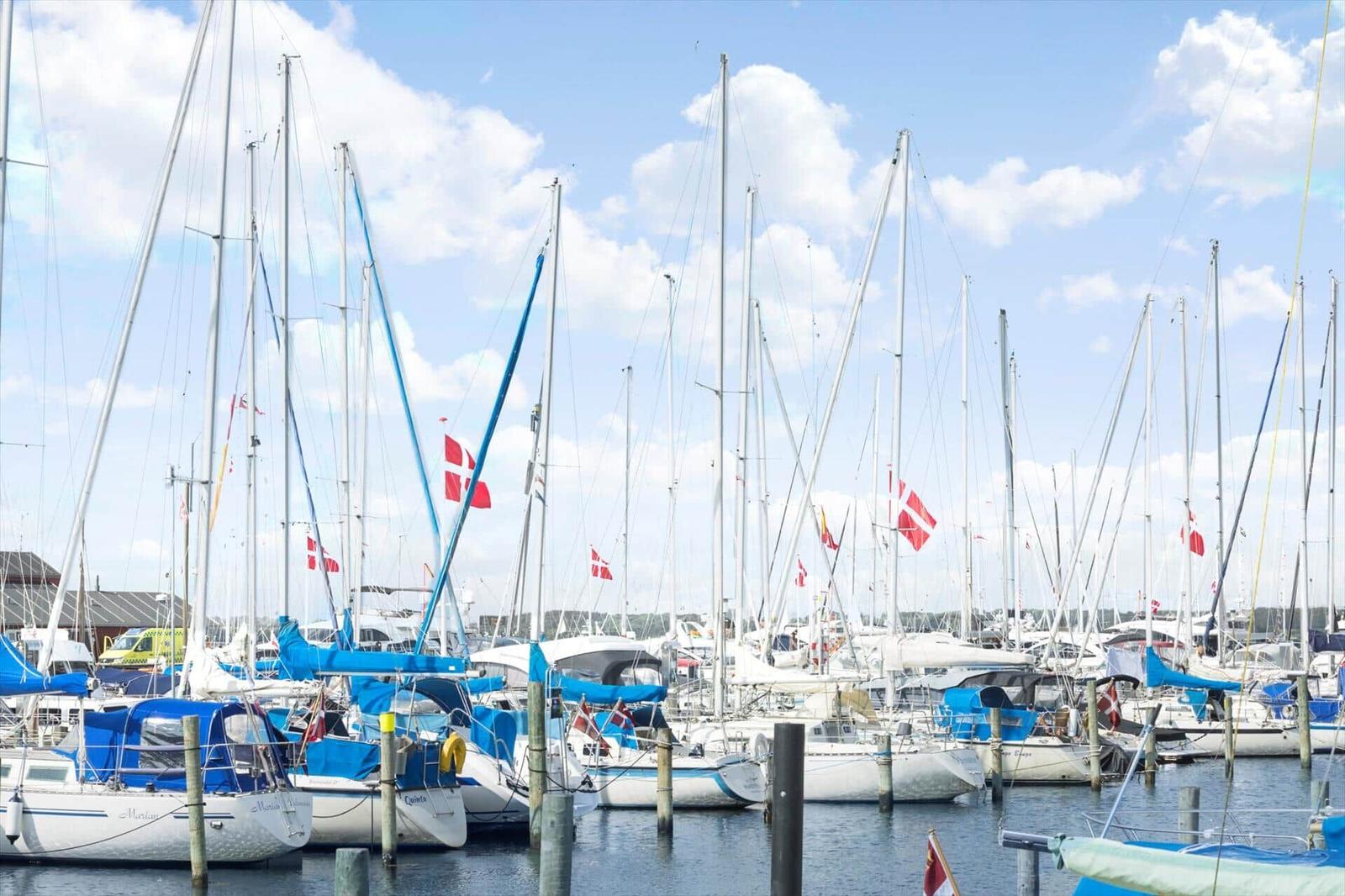 Sailboats with masts and Danish flags are docked. Blue sky with white clouds.