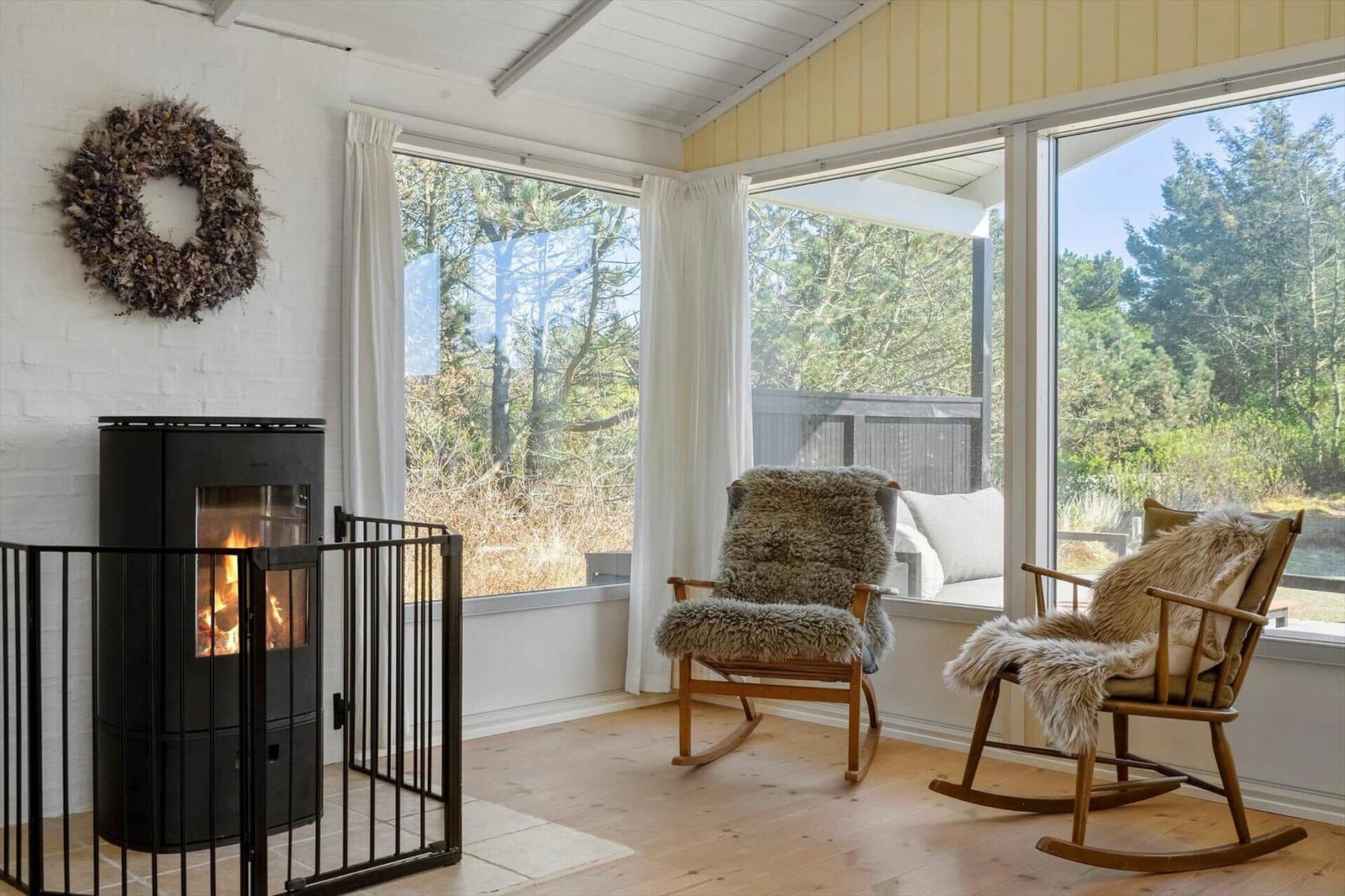 Raum mit Kamin, zwei Schaukelstühlen und großem Fensterblick auf Wald.