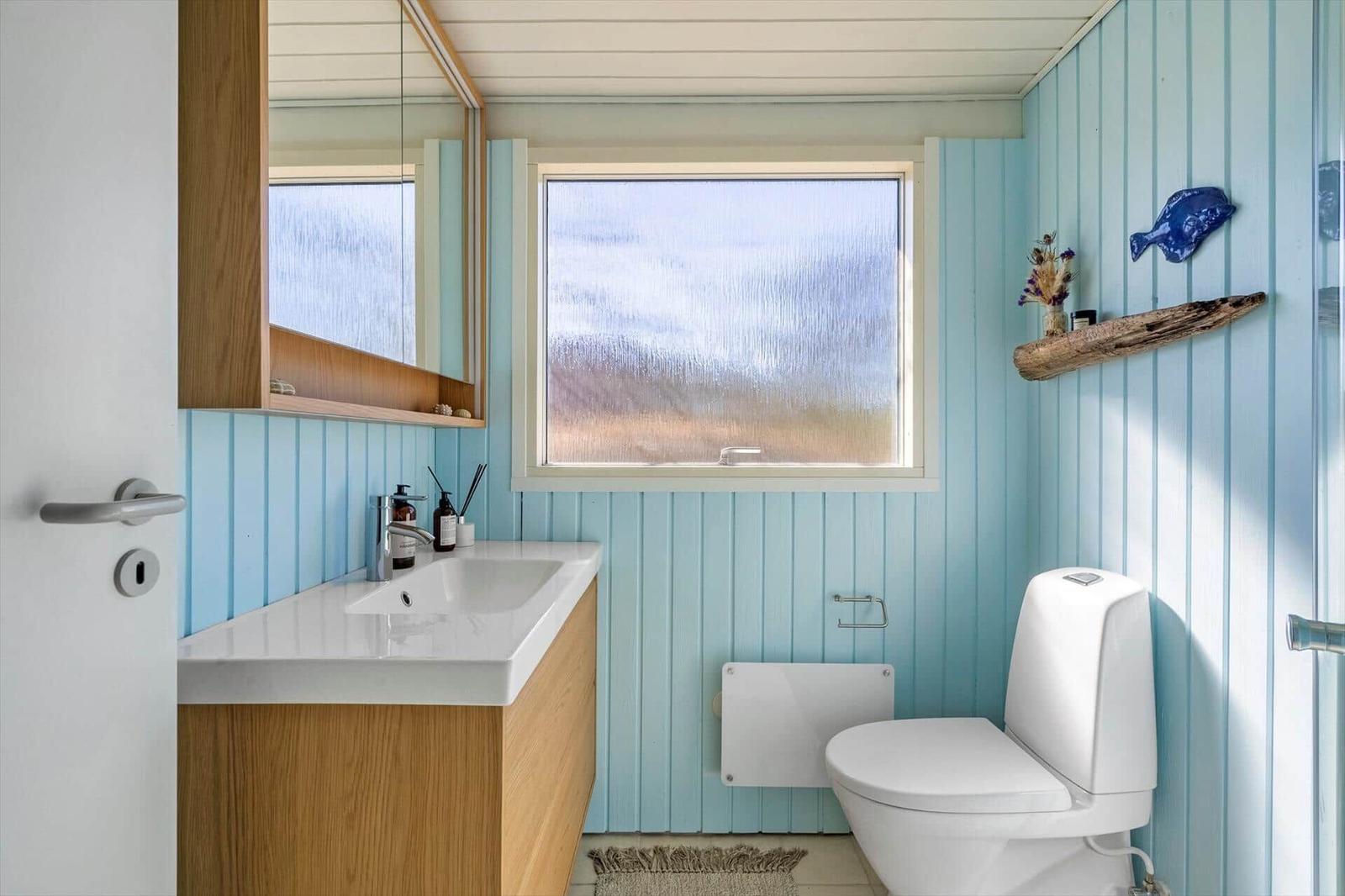 Badezimmer mit blauen Wänden, Waschbecken und Toilette. Fenster mit getöntem Glas.