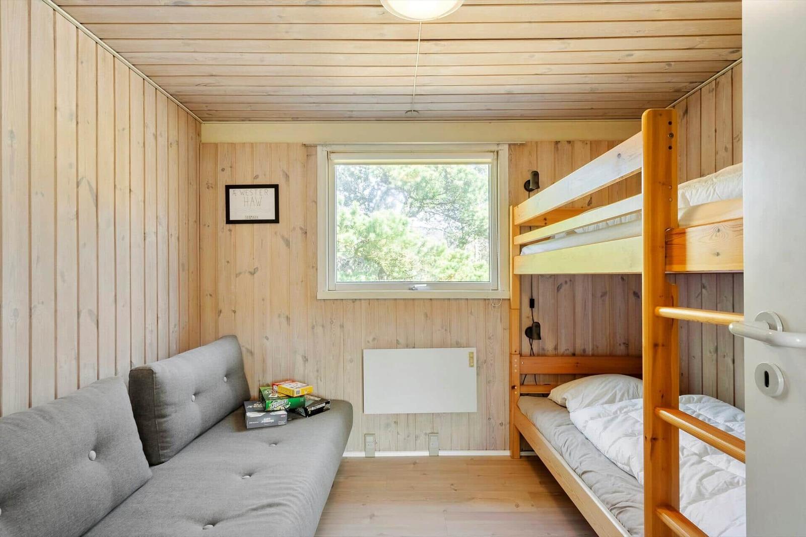 Zimmer mit Schlafcouch, Doppelbett und Fenster mit Blick auf Bäume.