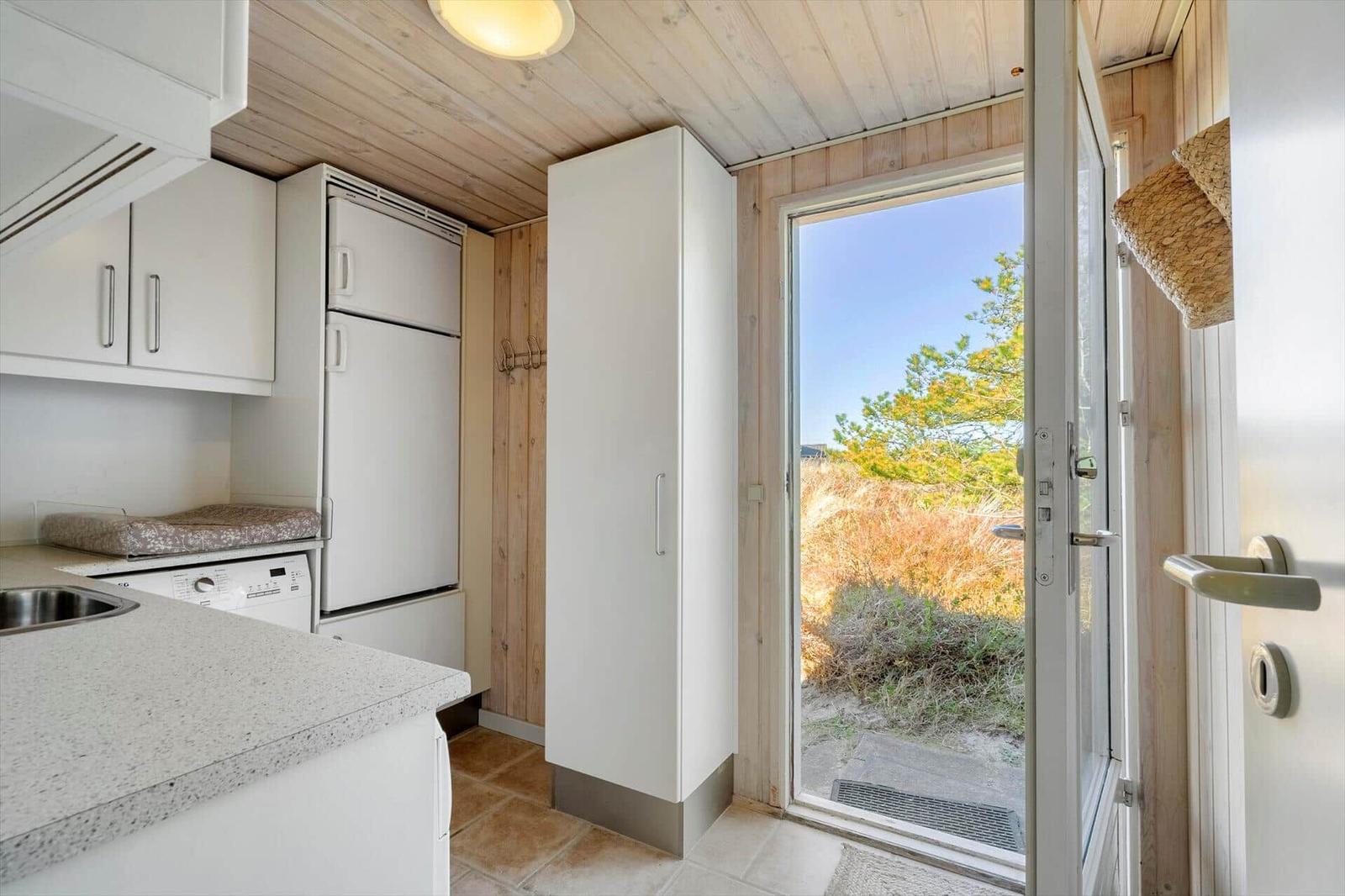 Küche mit weißen Schränken, Kühlschrank und Blick auf den Garten.
