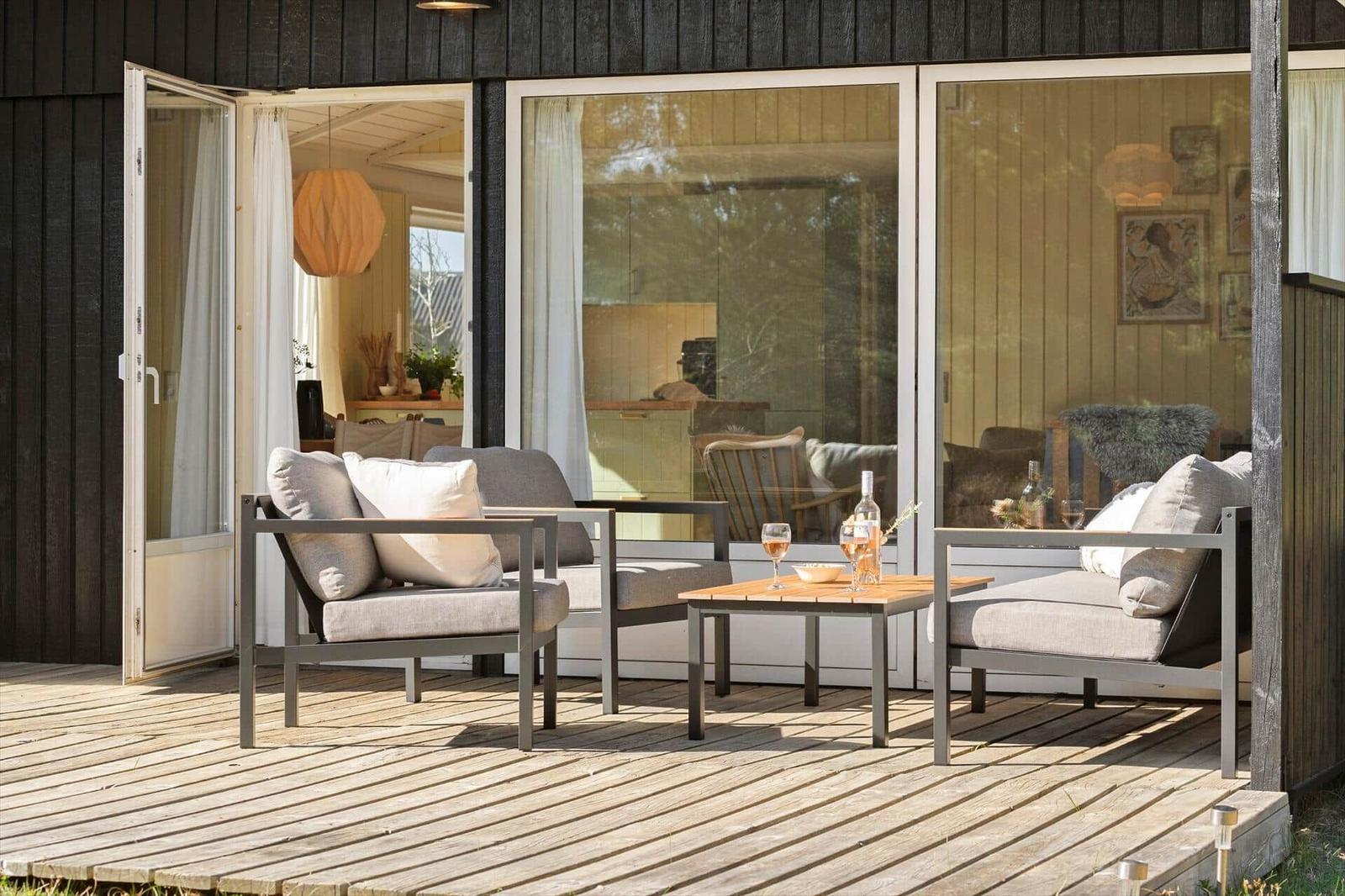 Terrasse mit zwei Sesseln und Tisch. Durchgehende Glastüren führen ins Innere.
