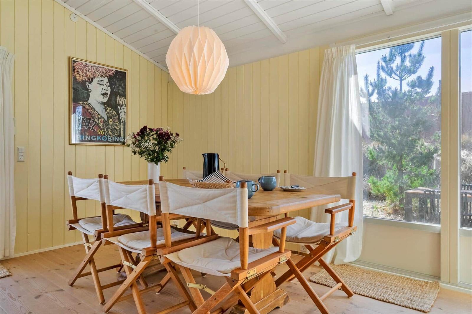 Esszimmer mit Holztisch, Stühlen und Fensterblick auf Bäume.