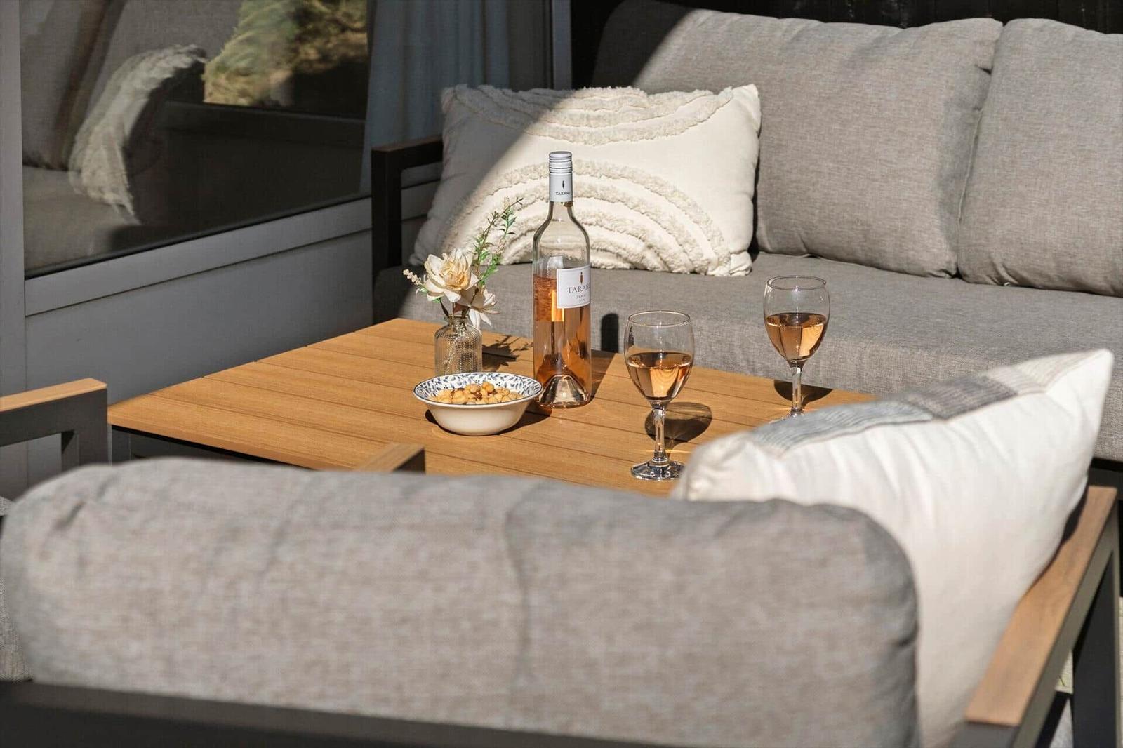 Außenbereich mit Sofa, Tisch und Flasche Roséwein. Auf dem Tisch stehen zwei Gläser und eine Schale mit Nüssen.