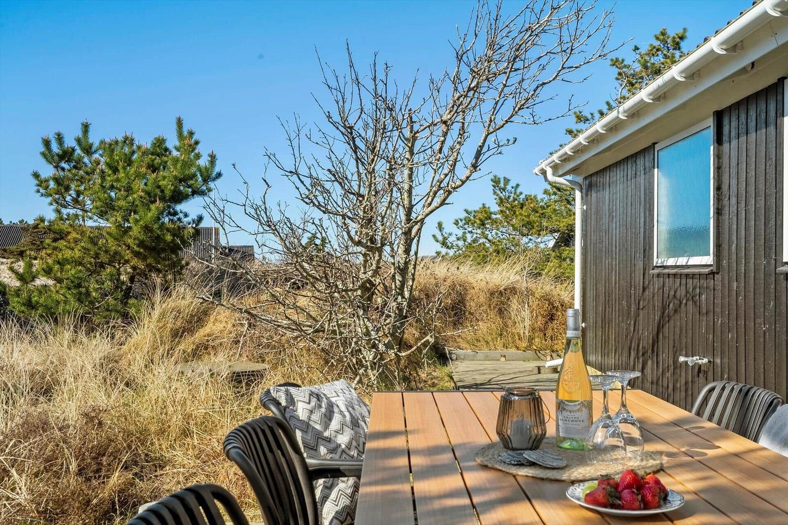 Holztisch mit Stühlen, Wein und Erdbeeren auf einer Terrasse neben einem Holzhaus.
