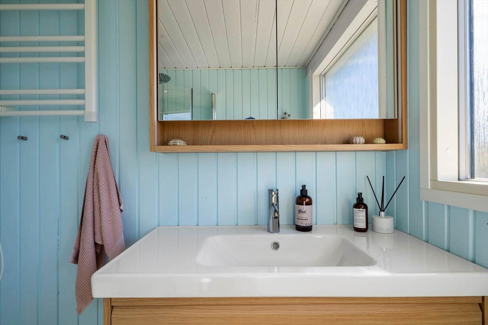 Badezimmer mit Waschbecken, Spiegel und Fenster. Wände sind hellblau verkleidet.