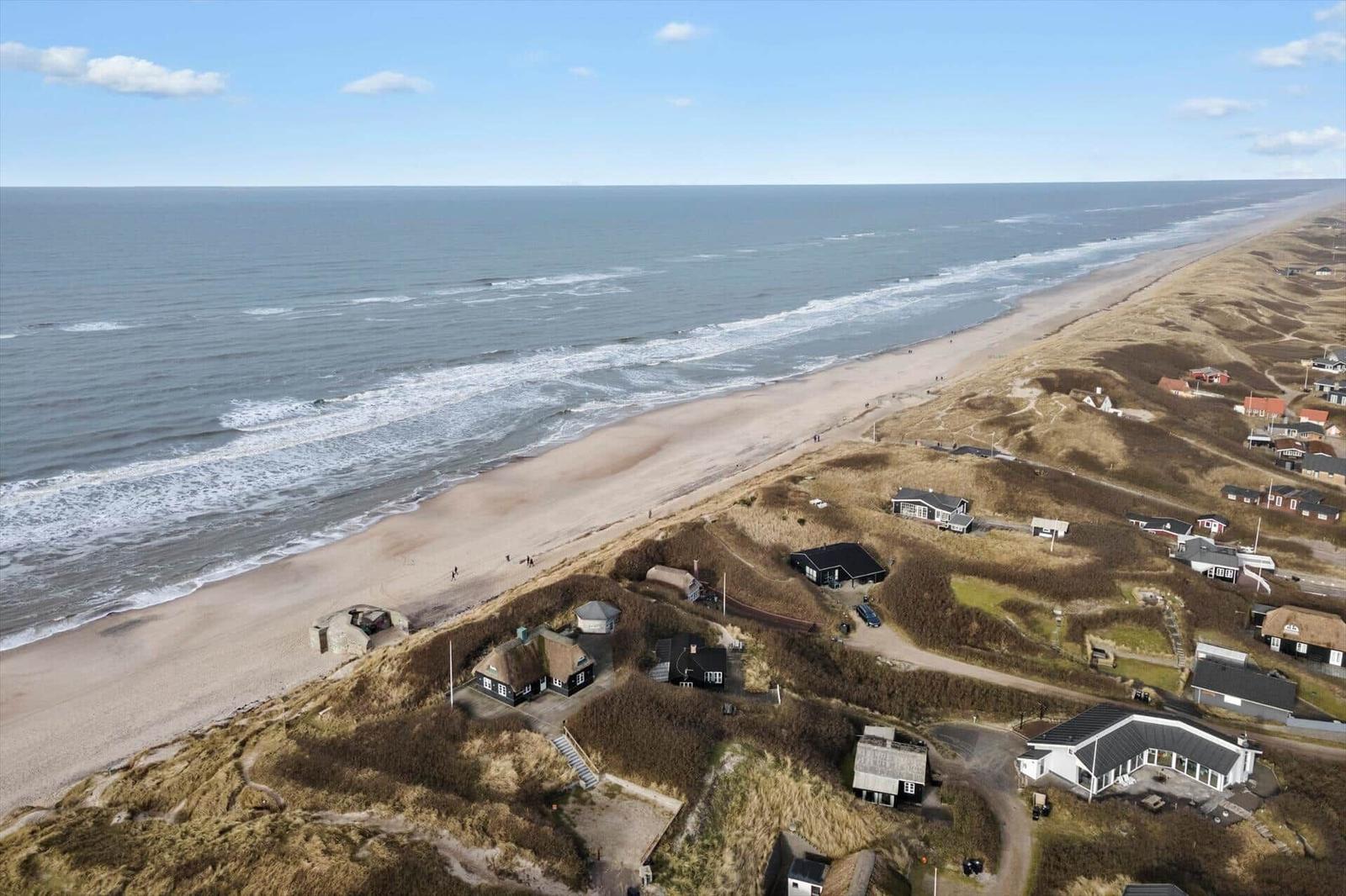 Aerielansicht von Strand und Dünen mit mehreren Häusern in der Nähe des Meeres.