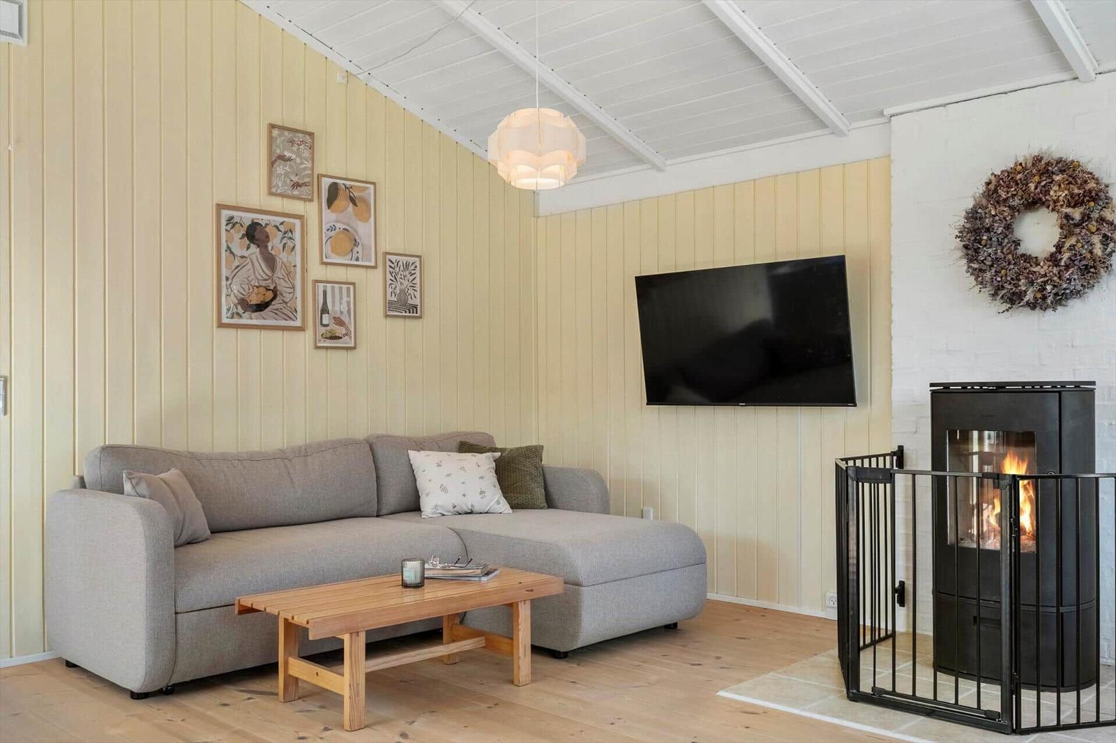 Wohnzimmer mit Sofa, Fernseher und Kaminofen an der Wand.