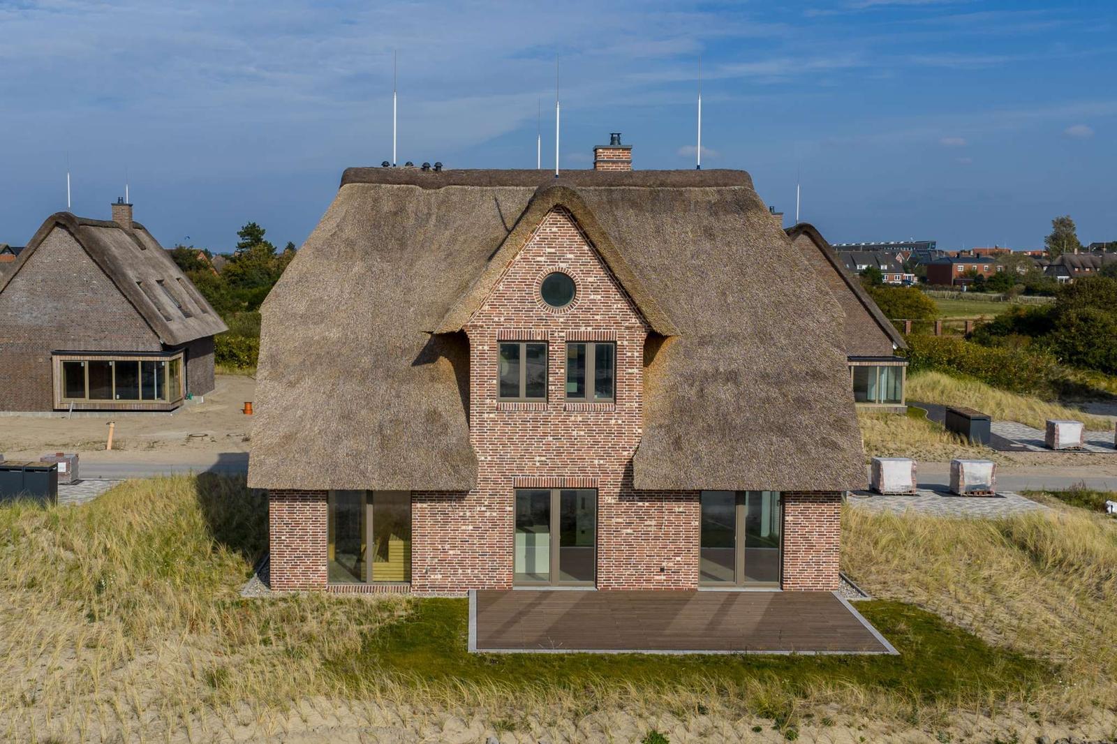 Haus mit Strohdach und Backsteinfassade auf Dünenlage