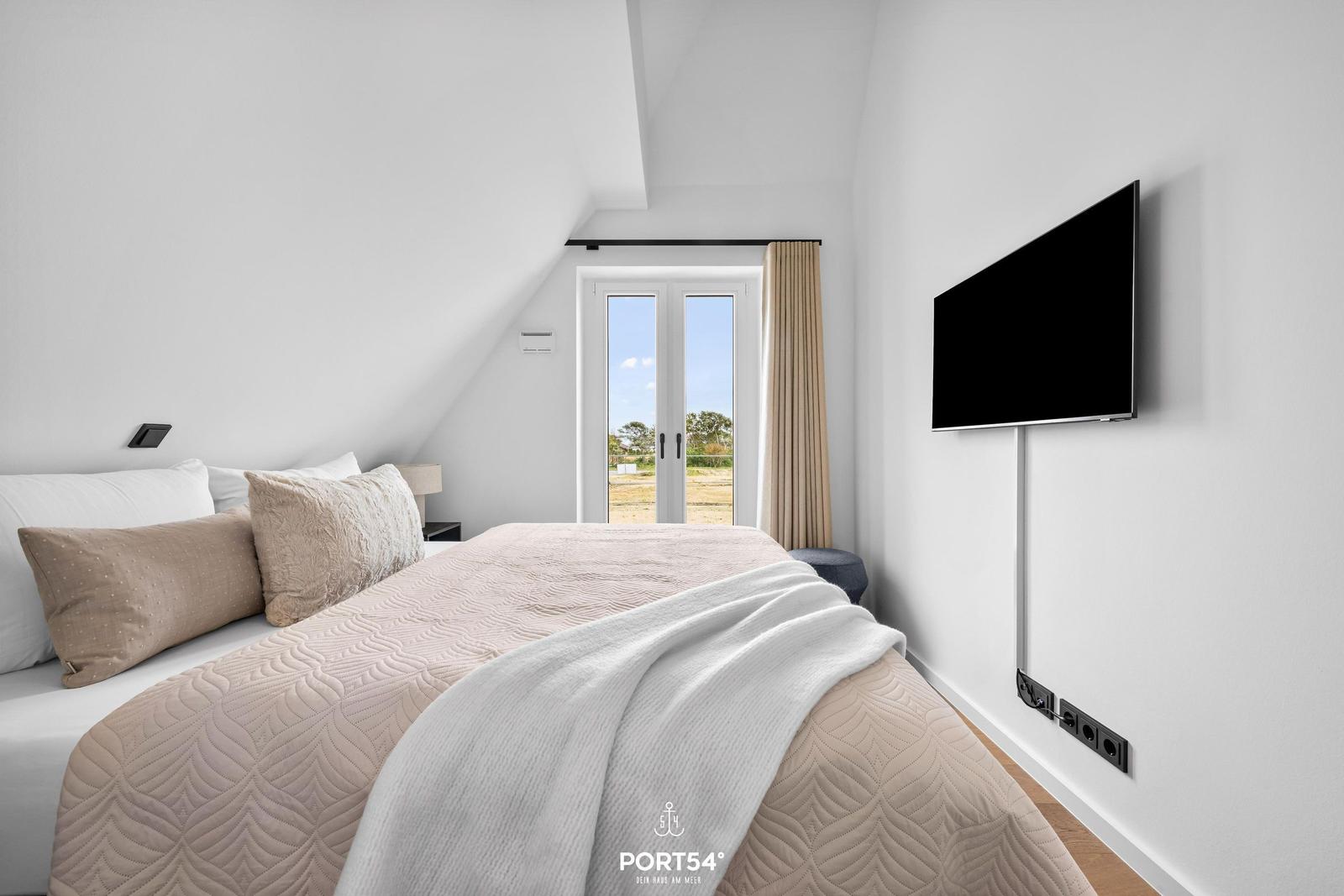Schlafzimmer mit Bett, TV und Fenster zur Außenseite.