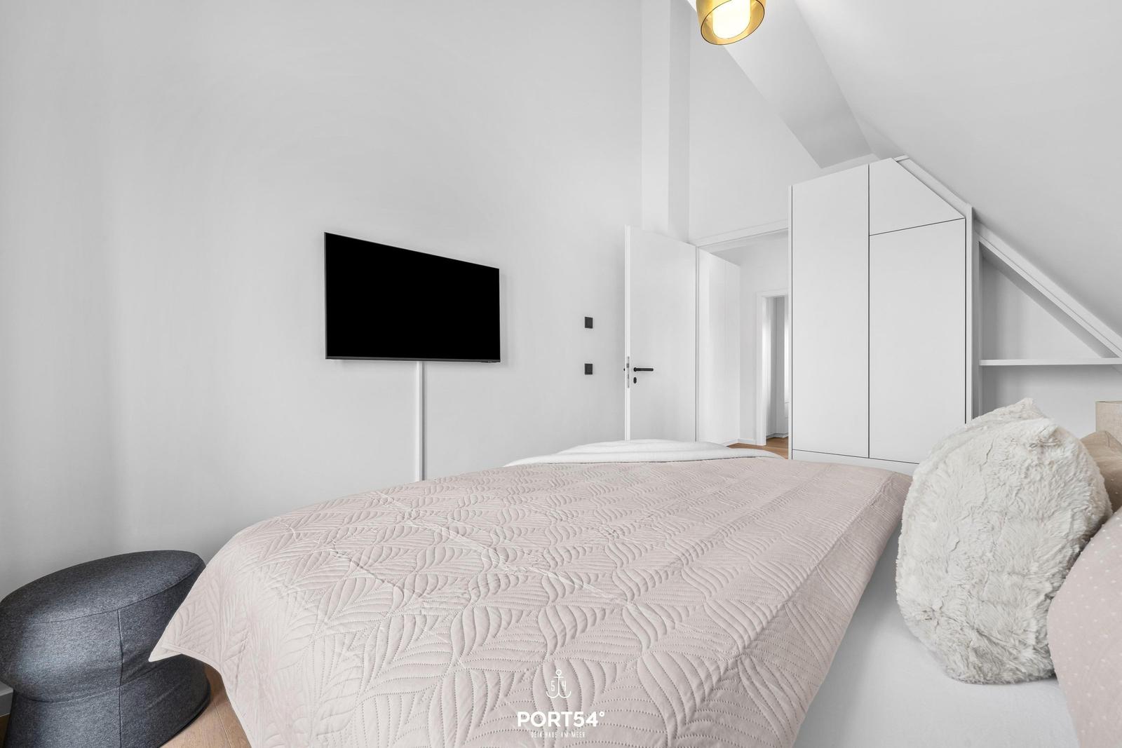 Schlafzimmer mit Bett, Fernseher und Kleiderschrank unter Dachschräge.